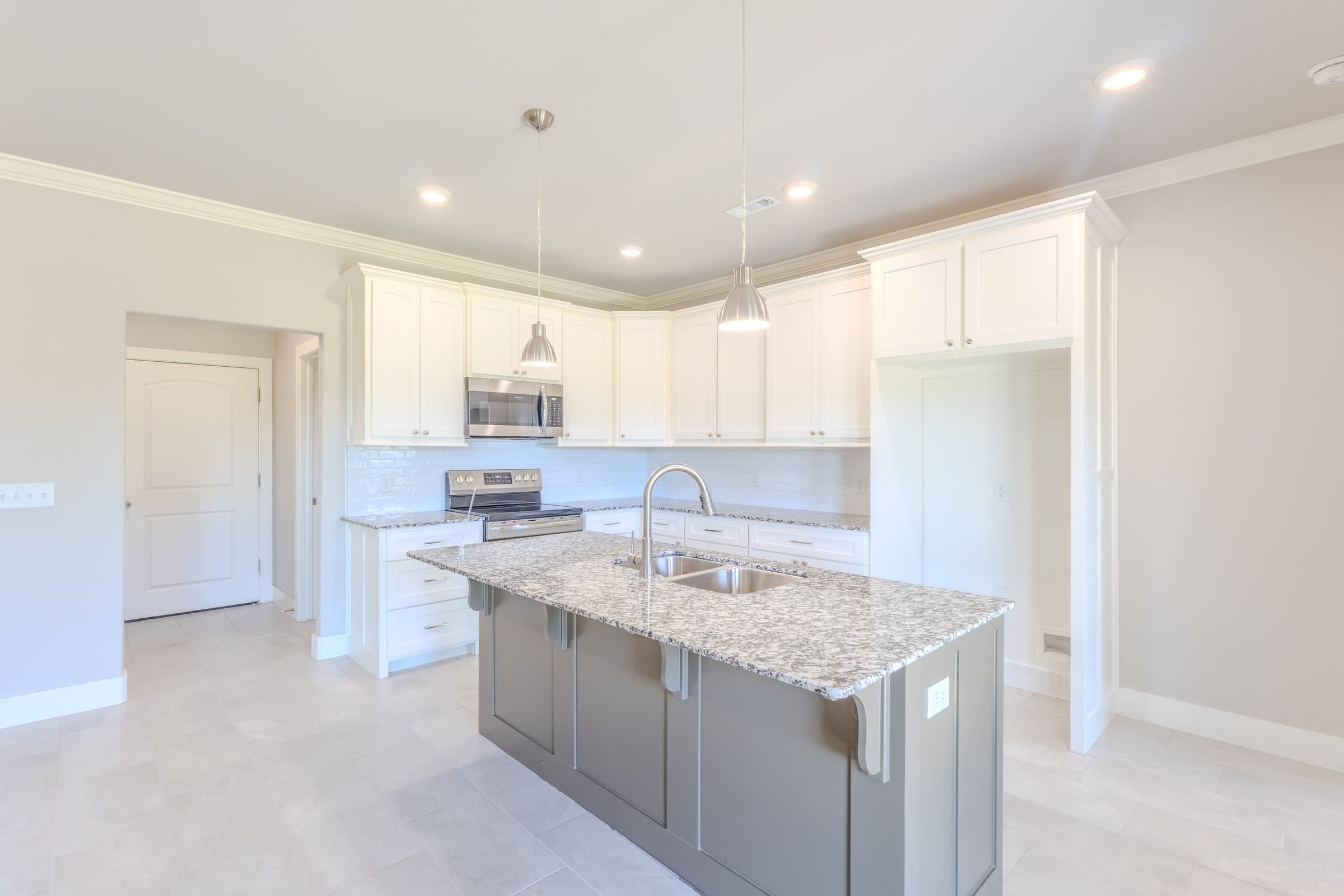 Gray kitchen island with a granite top under two pendant lights, white cabinets and a subway-tile backsplash behind it.