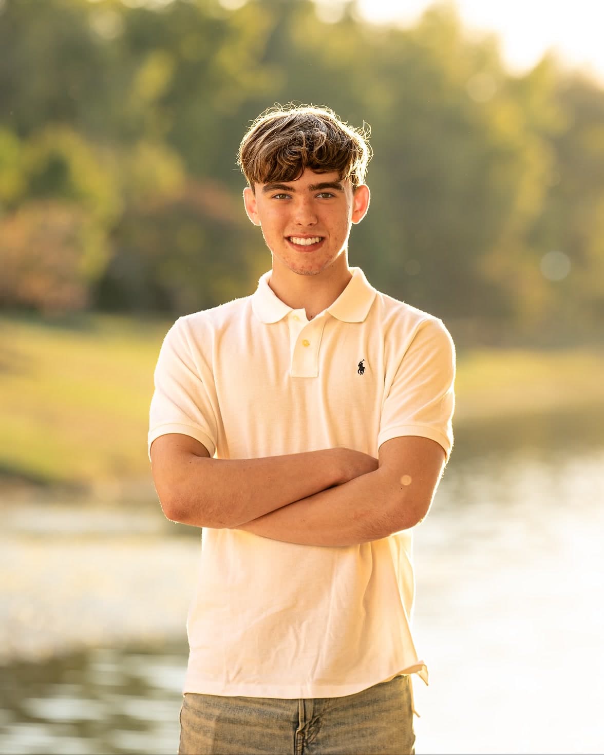 Chase Wright, owner of CWMedias, smiling with his arms crossed in a white polo, outdoors by a lake in evening light.